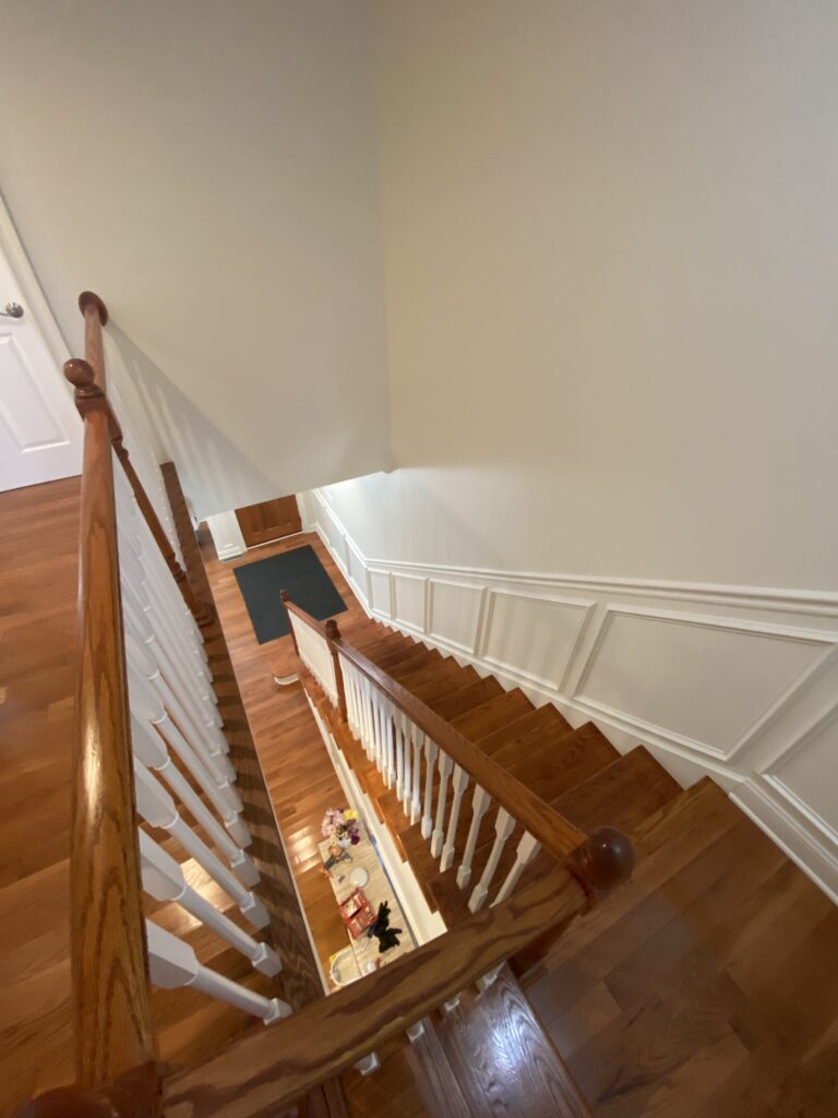 A view of a large stairway from the second floor to the ground floor, showcasing the freshly painted white walls and moldings