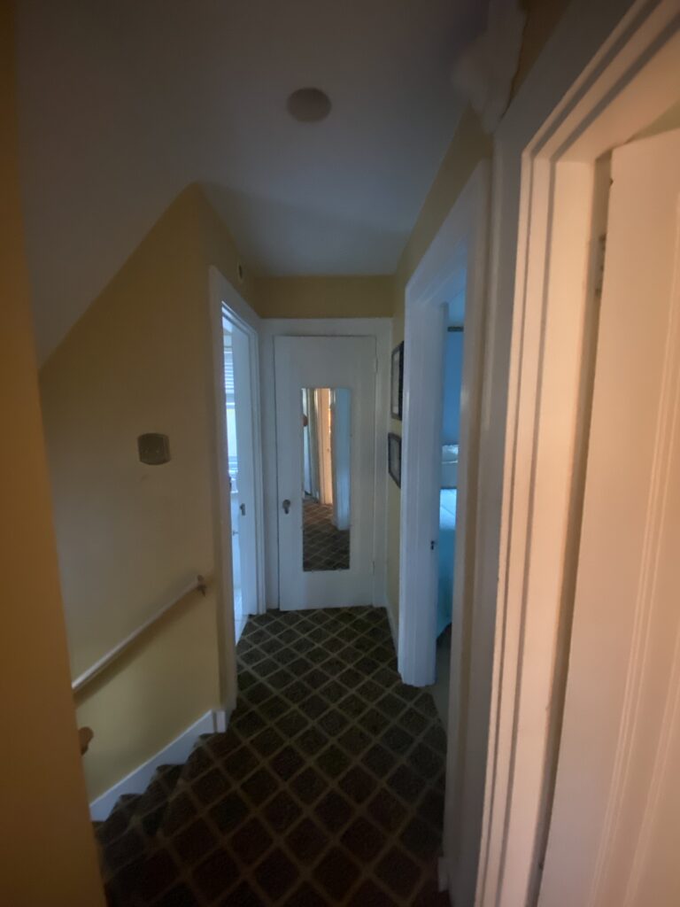 An image of second floor hallway that has a geometric line carpet, yellow painted walls and white painted celling and doors
